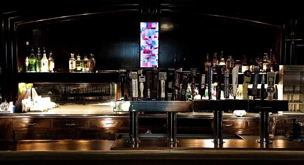 Well-stocked bar with glowing liquor bottles and numerous beer taps.
