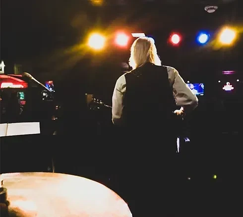 Musician playing guitar from behind on stage, colorful lights.