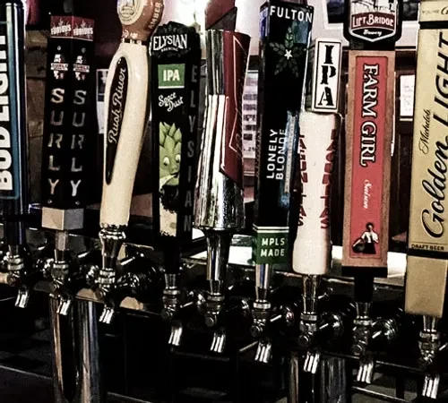 Close-up of various branded beer tap handles on a bar.