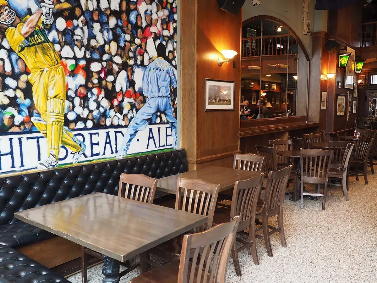 Pub interior with leather banquettes, wooden tables and cricket mural