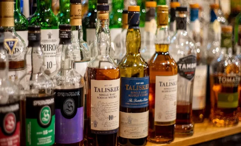 Close-up of various whisky and scotch bottles on a wooden shelf.