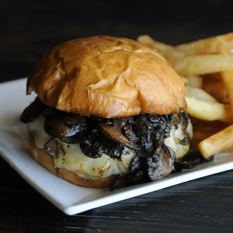 Gourmet burger with melted cheese, sautéed mushrooms, and french fries.