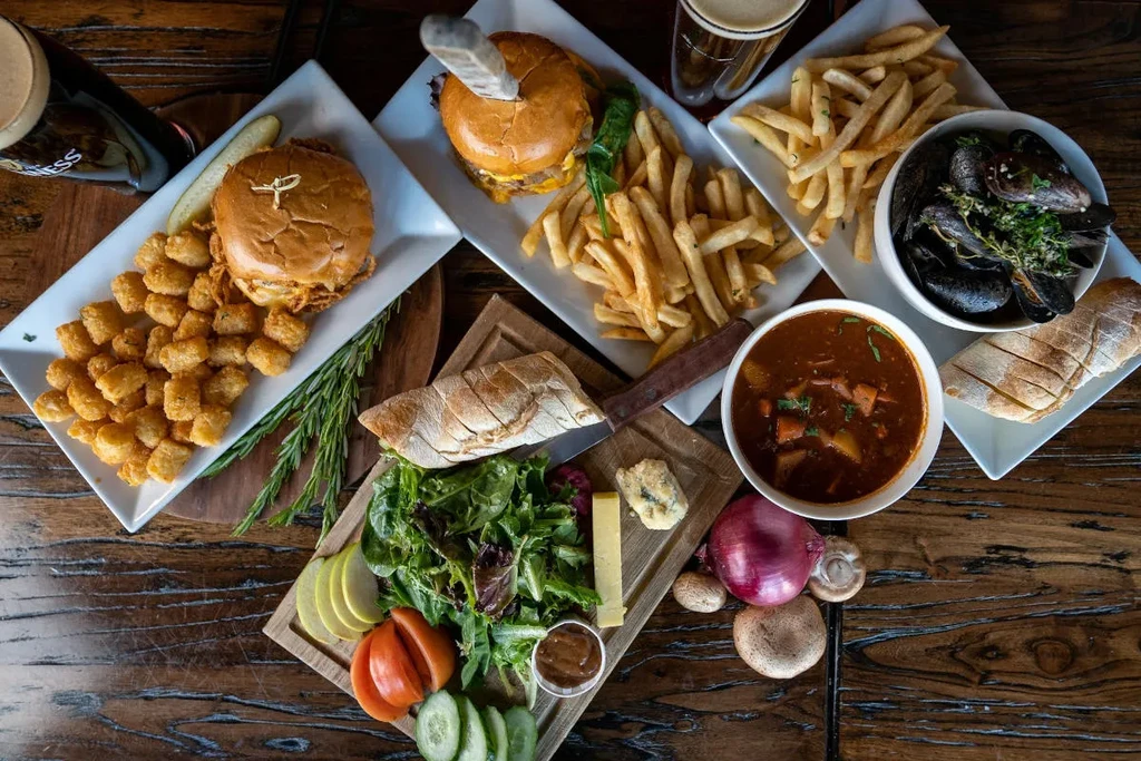 Overhead rustic table with burgers, mussels, stew, fries, and beers.