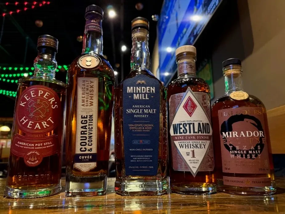 Five American single malt whiskey bottles on a bar counter.