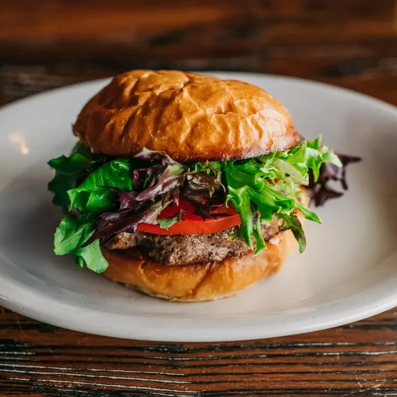 Hamburger with bun, patty, lettuce, tomato on a white plate.