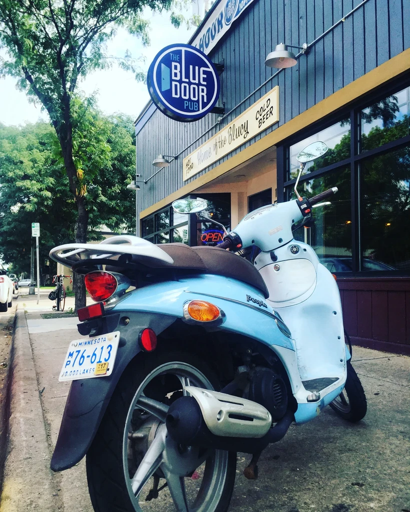 Light blue and white scooter parked in front of The Blue Door Pub.