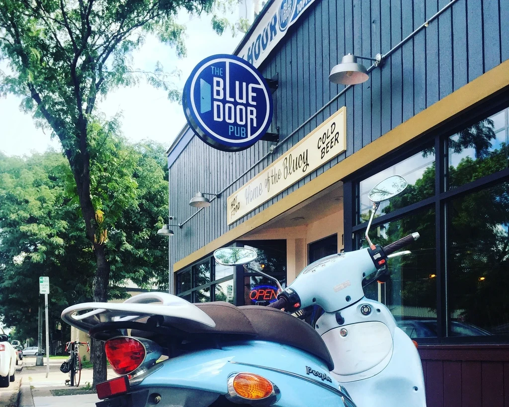 Blue scooter parked outside The Blue Door Pub on a bright day.