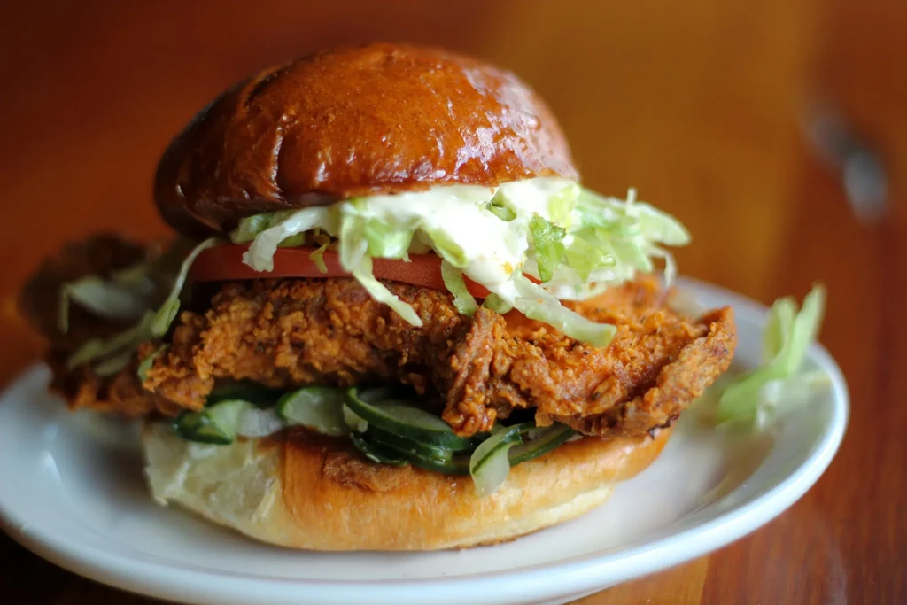 Crispy fried chicken sandwich on a plate with lettuce, tomato, pickles.