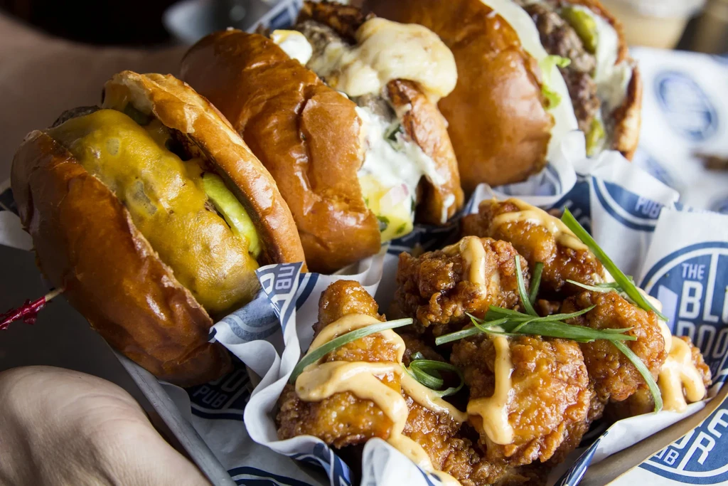 Three sandwiches with melted cheese and fried chicken in a pub basket.