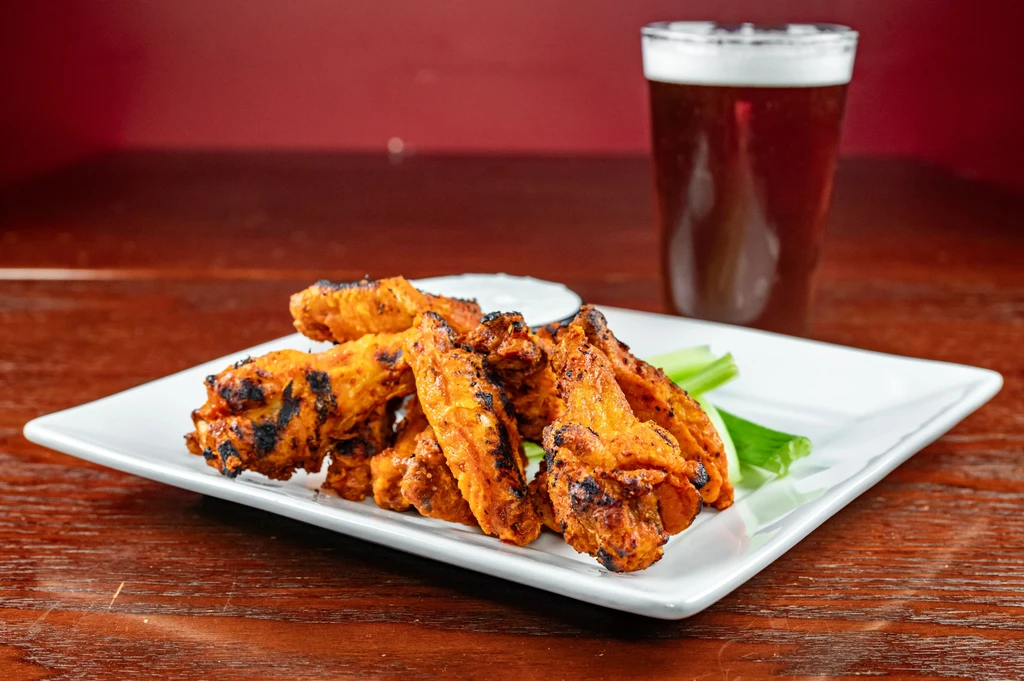 Golden chicken wings, sauce, celery, and beer on a platter.