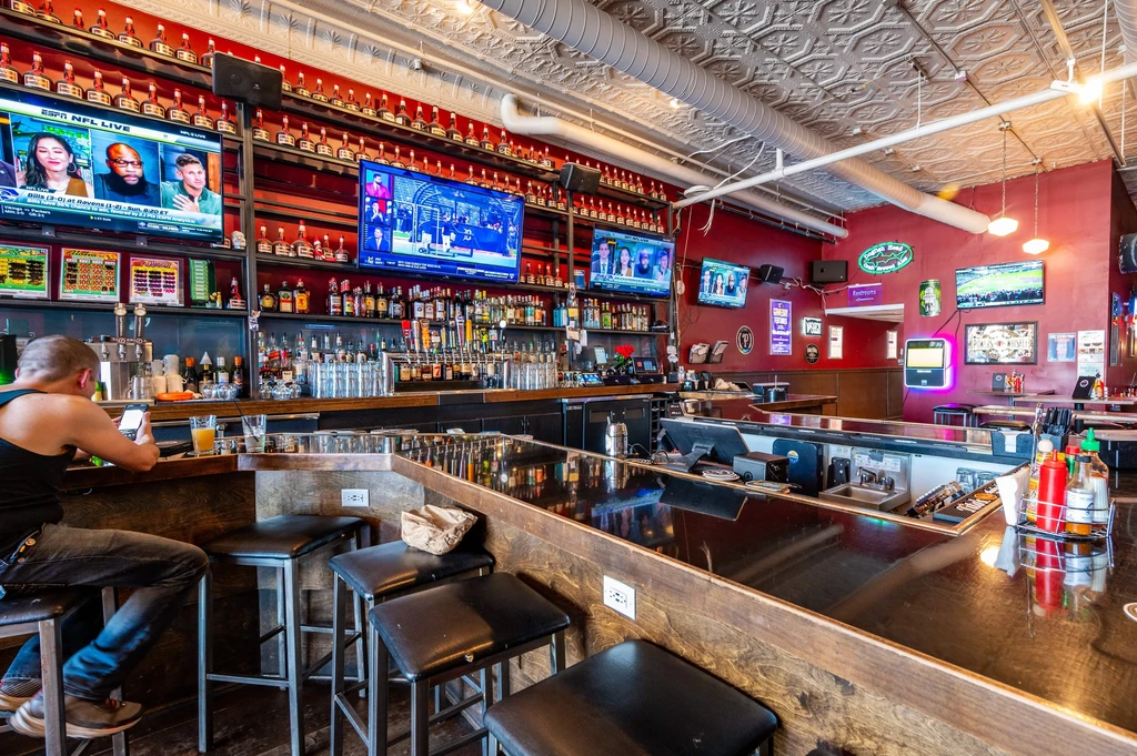 Vibrant sports bar interior with dark bar, TVs, and drinks.
