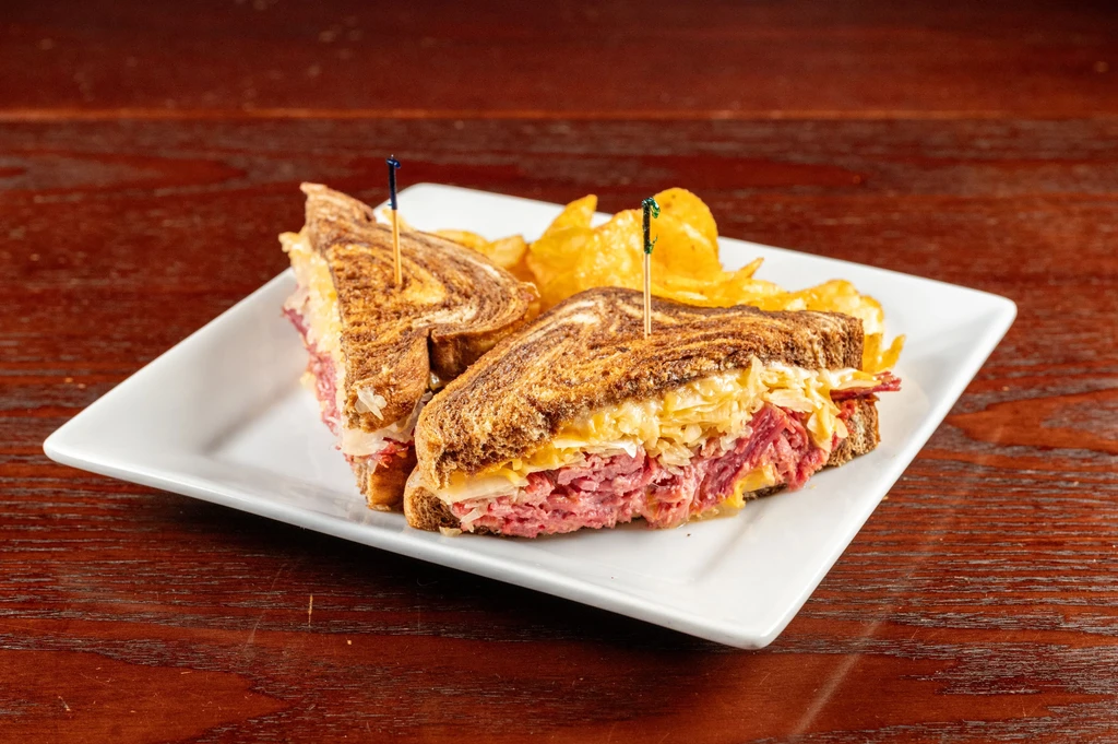 Deli sandwich halves with toothpicks and chips on a white plate.