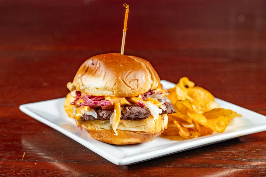 Gourmet double-patty slider with cheese, onions, and chips on a plate.