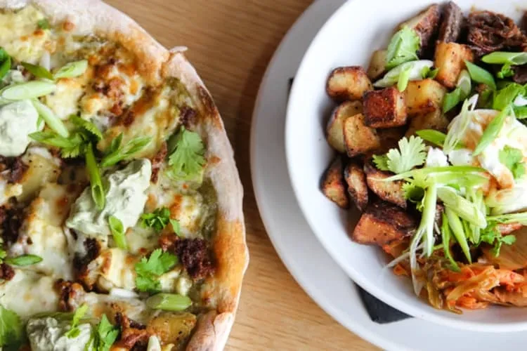 Flatbread and roasted potatoes in a bowl, garnished, on wood.