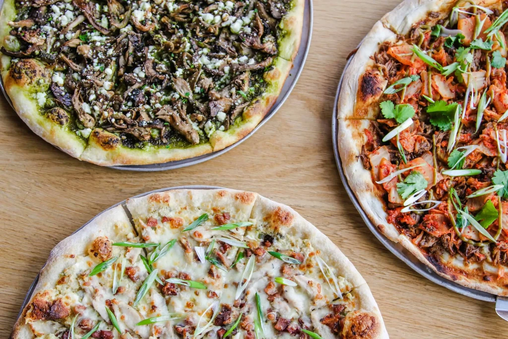 Three distinct pizzas: pesto, chicken, and kimchi-topped.