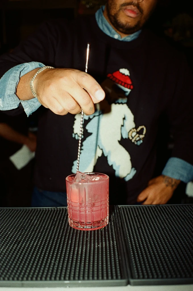 Bartender's hands stirring a pink cocktail, wearing a yeti shirt.