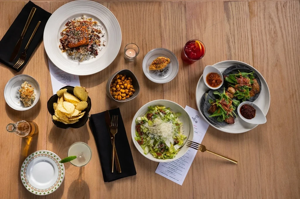 Overhead view: wooden table with salmon, tacos, salad, drinks, and appetizers.