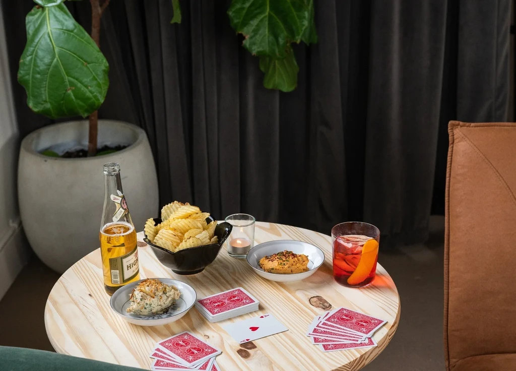 Beer, chips, dips, and playing cards on a table with a lit candle.