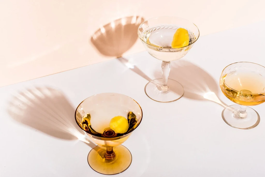 Three cocktails with garnishes on a diagonal peach and white wall.