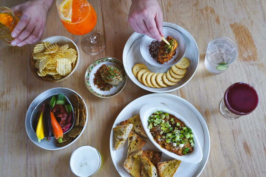 Wooden table laden with appetizers, dips, drinks, and interacting hands.