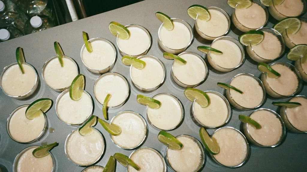 Dozens of creamy frozen cocktails with lime wedges on a grey surface.