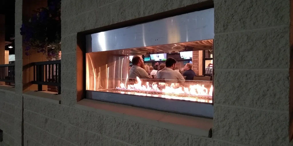 Restaurant window with gas fireplace, bright flames, and patrons inside.