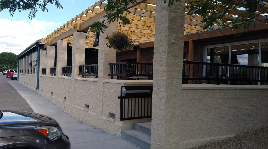 Bright restaurant patio with stone pillars, wooden pergola, and string lights.