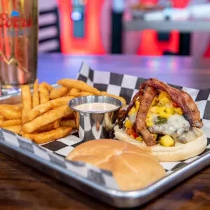 Open-faced burger with melted cheese, bacon, fries, and dipping sauce.