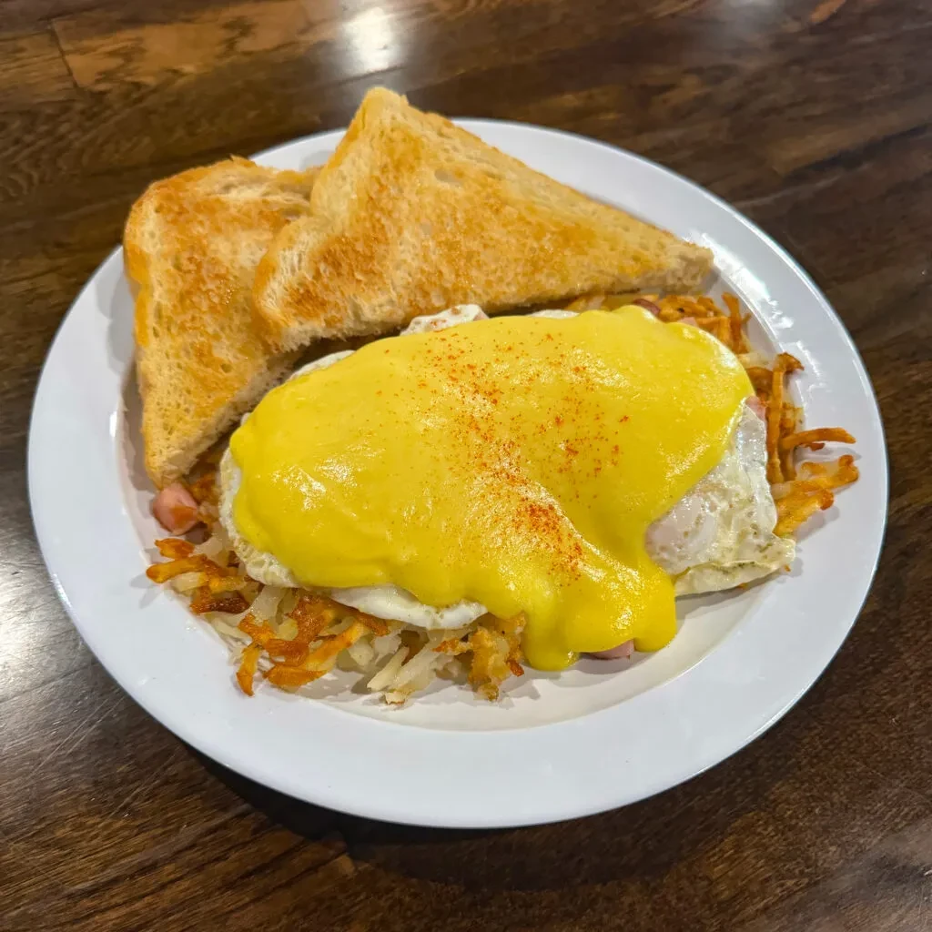Eggs Benedict, ham, hash browns, and toast on a dark wooden table.