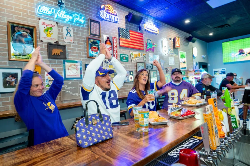 Excited fans in purple and gold jerseys cheering at a lively sports bar.