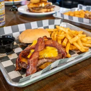 Loaded open-faced bacon cheeseburger with fries and dipping sauce.