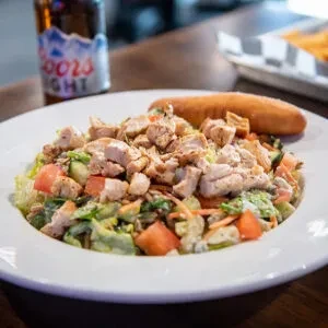 Chicken salad with breadstick on a plate, blurred beer in background.