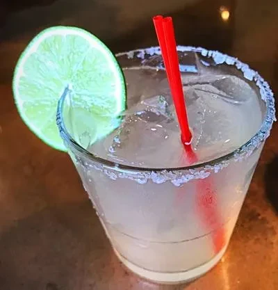 A margarita with ice, salted rim, lime wheel, and red straw.