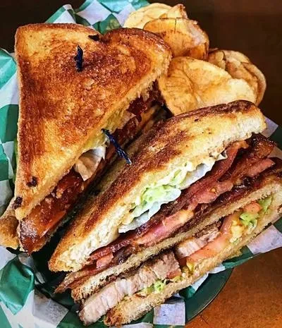 Grilled sandwich with bacon, lettuce, tomato, meat, and potato chips.