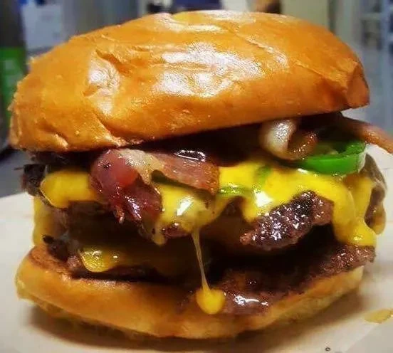 Close-up juicy double cheeseburger with melted cheese, caramelized onions and jalapeños.