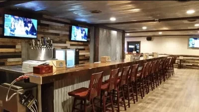 Rustic bar with corrugated metal front, beer taps, and sports TVs.