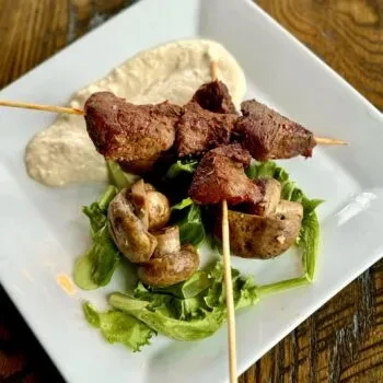 Grilled meat skewers on lettuce with mushrooms and creamy dip.