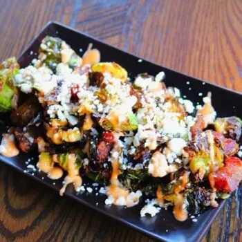 Roasted Brussels sprouts with crumbled cheese, orange sauce, and bacon.