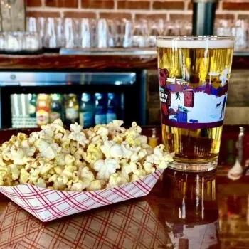 Popcorn in a checkered boat and a glass of beer on a bar.