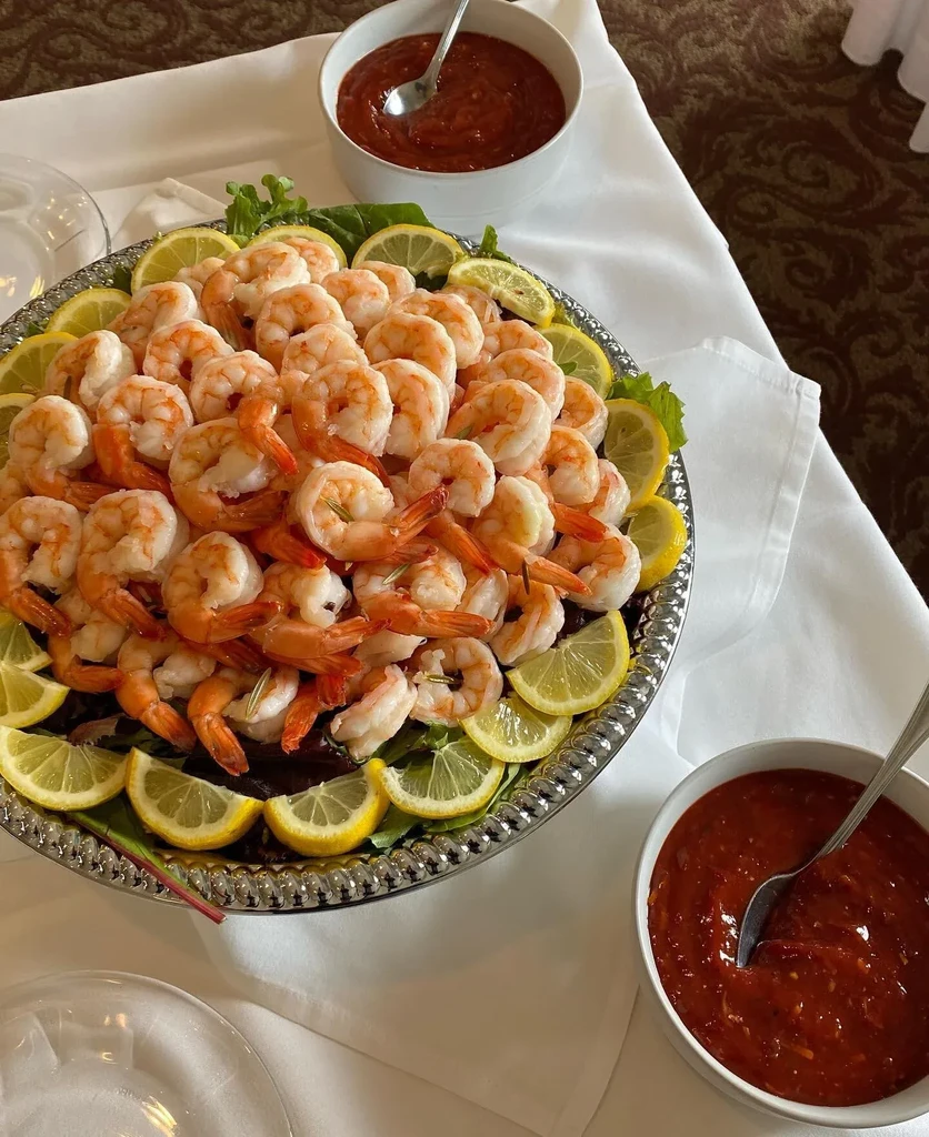 Silver platter of shrimp cocktail with lemon and cocktail sauce.