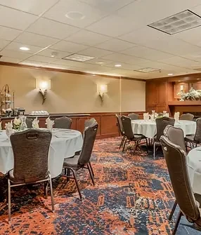 Banquet hall with round tables, buffet, fireplace, and patterned carpet.