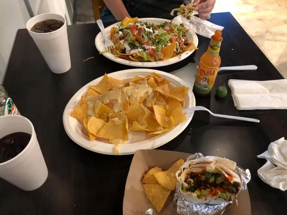 Person eating loaded nachos, cheese nachos, a burrito, and drinks.
