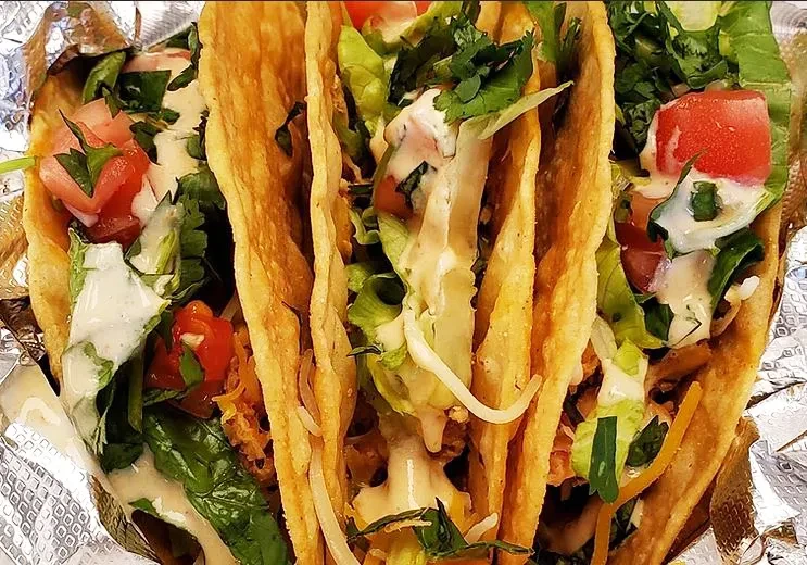 Three hard-shell tacos with meat, vegetables, and sauce, in foil.