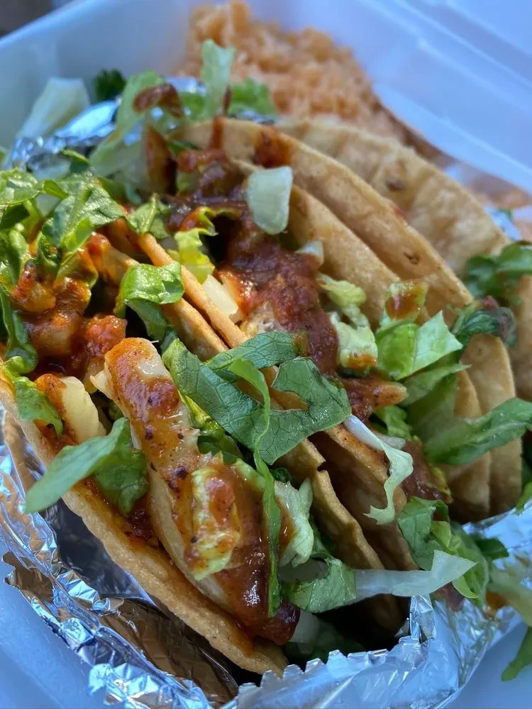 Takeout container of hard-shell tacos topped with lettuce, salsa, and rice.