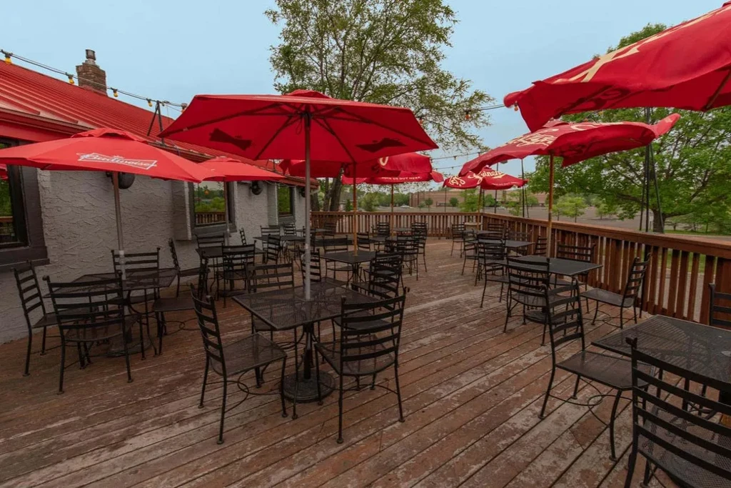 Empty restaurant patio with black tables, red branded umbrellas.