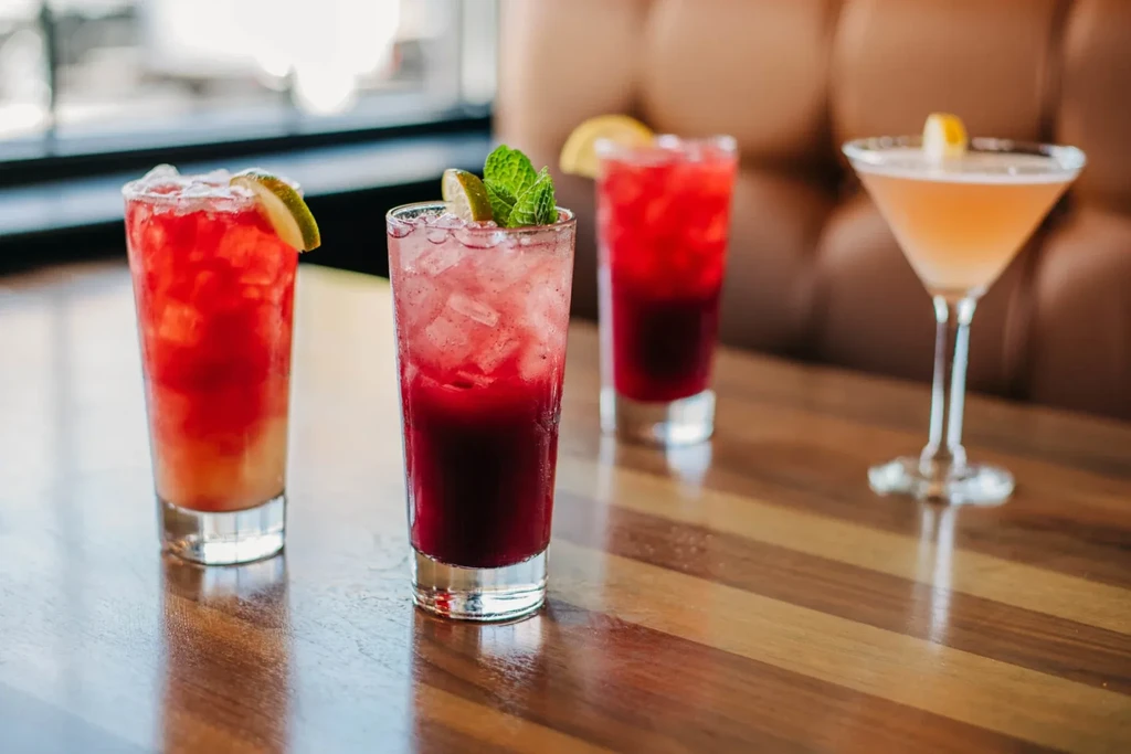 Four vibrant, garnished cocktails on a polished wooden table.