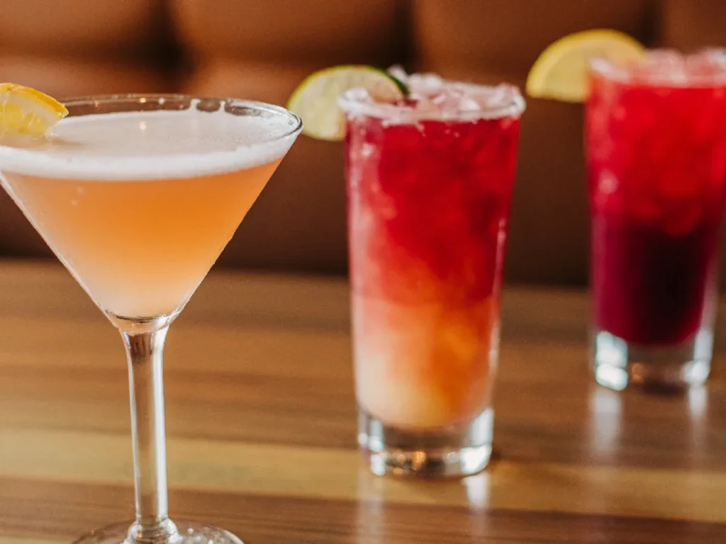 Three colorful cocktails in a martini glass and two tall glasses on wood.