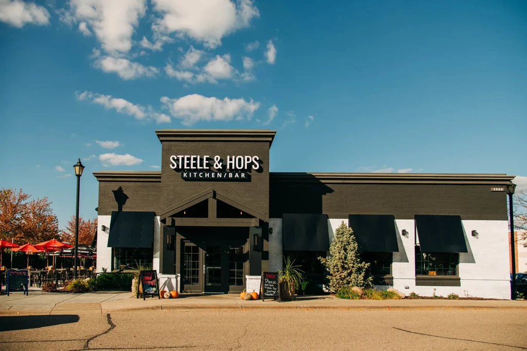 STEELE & HOPS KITCHEN/BAR exterior, patio with red umbrellas, autumn decor.