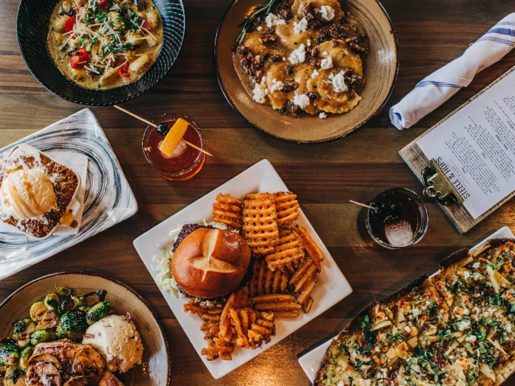 Overhead shot: Wooden table with restaurant food, drinks, and "STEELE & HOPS" menu.