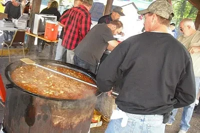 Large pot of steaming stew stirred outdoors at a communal event.